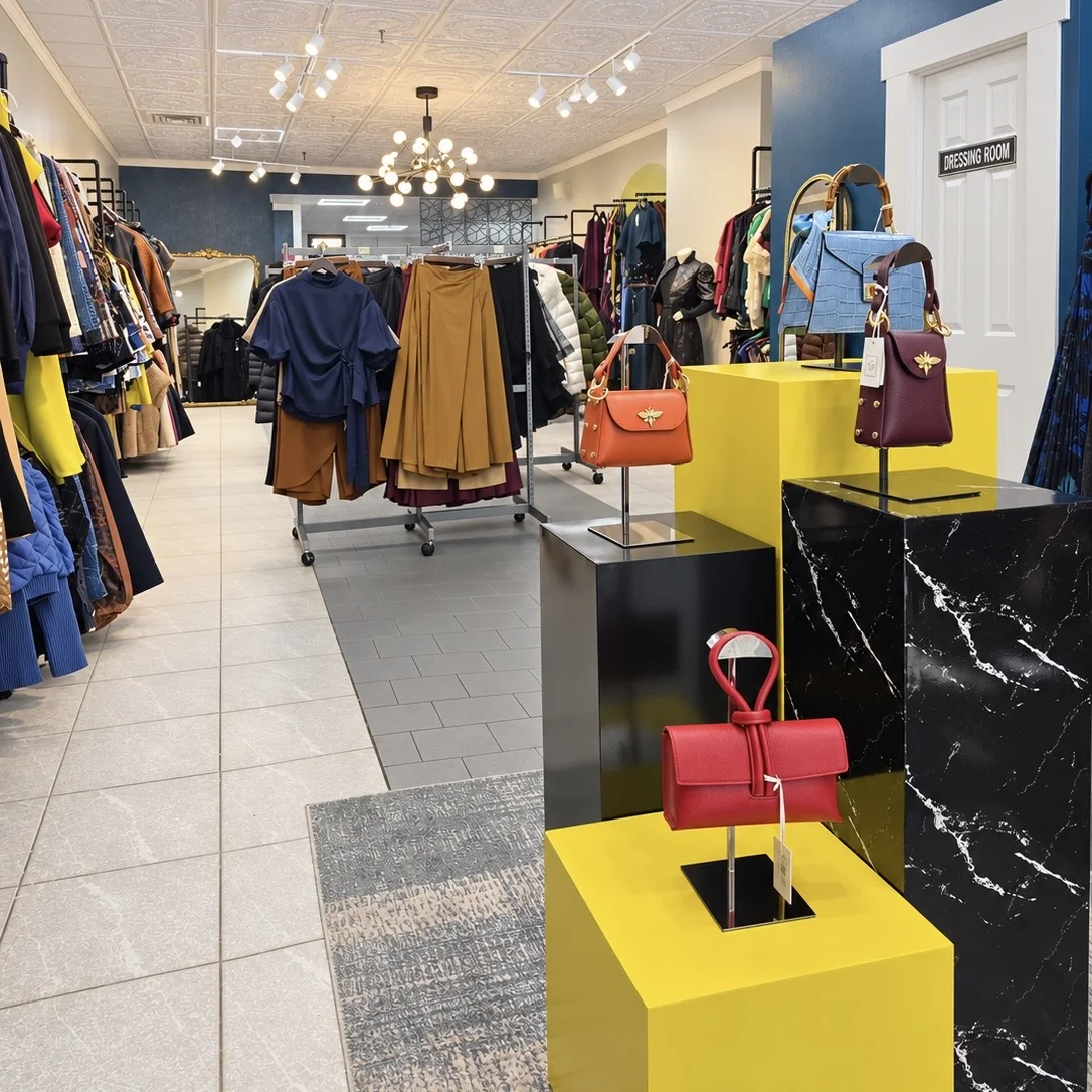 Colorful handbags displayed on yellow and black plinths beside the boutique clothing selection